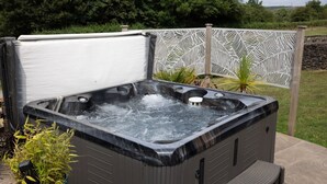 A hot tub with multiple seating areas, surrounded by a decorative fence and greenery. - The Granary 3 bedroom  cottage (Porthcawl)