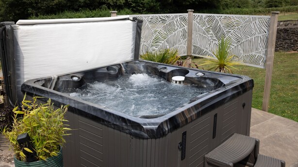 A hot tub with a waterfall feature, surrounded by a decorative fence and potted plants. - The Granary 3 bedroom  cottage (Porthcawl)