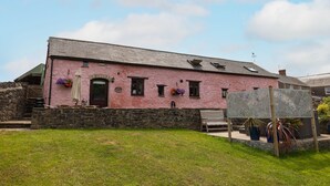 A pink building with a stone wall, a wooden bench, and a metal fence. - The Granary 3 bedroom  cottage (Porthcawl)