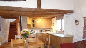 A cozy kitchen with wooden cabinets, a dining table with chairs, and a red sofa. - The Granary 3 bedroom  cottage (Porthcawl)