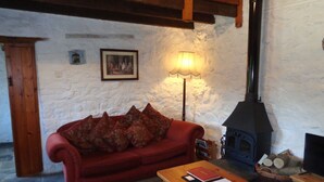 A cozy living room with a red sofa, a wooden coffee table, a patterned rug, a fireplace, and a wall-mounted lamp. - The Granary 3 bedroom  cottage (Porthcawl)