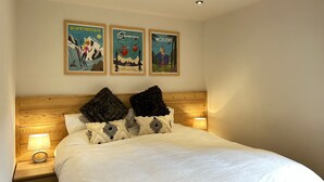 Un dormitorio con cabecera de madera, cama blanca y tres carteles en la pared.