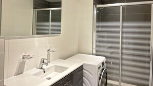 Un baño moderno con un espejo grande, dos lavamanos, una ducha con puerta de vidrio y un inodoro.
