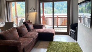 Una sala de estar moderna con un sofá de cuero marrón, un tapete verde y un ventanal con vistas a un área boscosa.