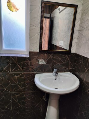Un baño con un lavabo blanco, un espejo con marco de madera y una ventana con vista a un árbol.