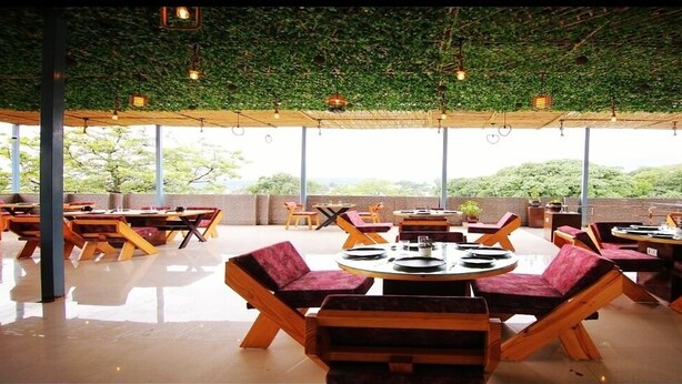 Un restaurante al aire libre con mesas redondas y asientos acolchados, rodeado de amplias ventanas que ofrecen vistas del paisaje.