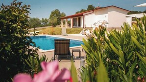 Una piscina con una sedia a sdraio, immersa nel verde e affiancata da un edificio con tetto rosso.