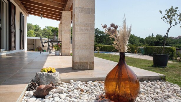 Un'area patio con un pilastro in pietra, un vaso grande con pampas secchi e un rustico vaso in pietra con un pigna e un vaso di terracotta.