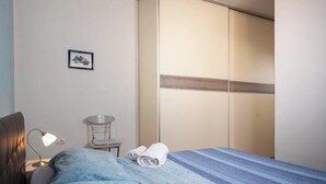 Una camera d'albergo con un letto, una scrivania con una lampada, una sedia, un armadio e un piccolo quadro appeso al muro.