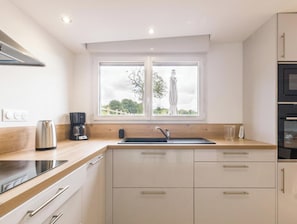 A modern kitchen with a window, stainless steel kettle, coffee maker, and built-in oven.