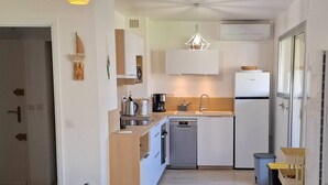 A compact kitchen with a dishwasher, sink, and a small refrigerator. There is a dining area with a table and chairs, and a colorful striped bedspread. - Cozy 3-Room Apartment with Balcony, Garage, Near Golf - Le Lavandou (Le Lavandou)