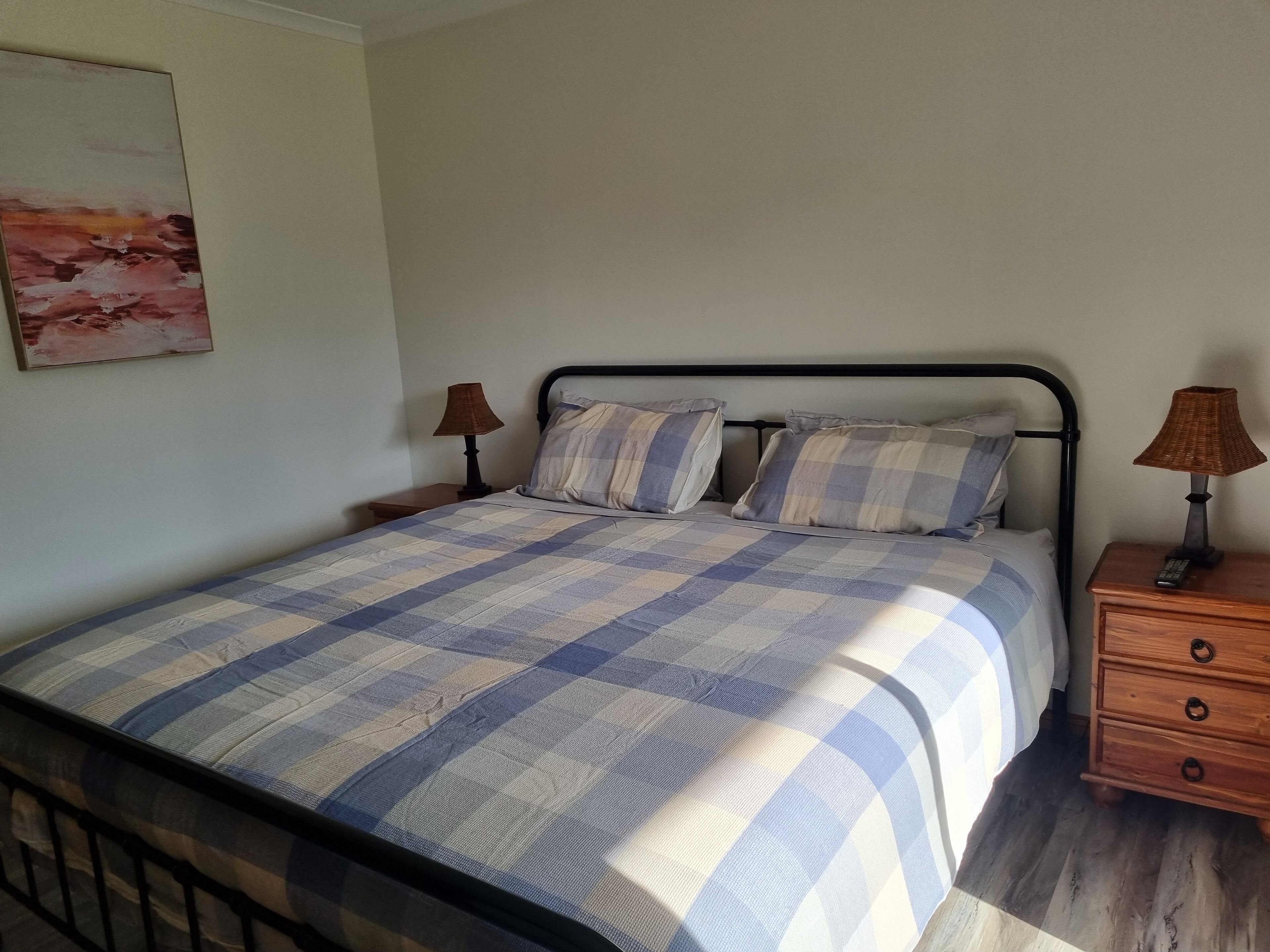A bedroom with a bed, two nightstands, a lamp on each nightstand, and a painting on the wall.
