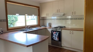 A kitchen with a wooden countertop, a built-in oven, and a window with blinds. - By the Beach (Apollo Bay)