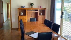 A dining area with a wooden table, black chairs, a wooden cabinet with glass doors, and a potted plant. - By the Beach (Apollo Bay)