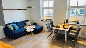 En moderne stue med en blå sofa, et rundt bord og et spiseområde med et træbord og stole.