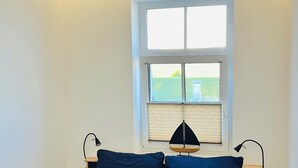Et soveværelse med seng, to sengeborde, et vindue der viser grønne omgivelser, og et loft med ovenlys.