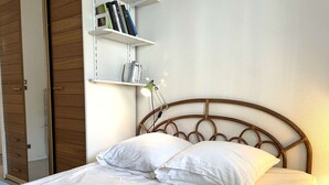 Una cama bien tendida con sábanas blancas, cabecero de madera y una lámpara de noche.