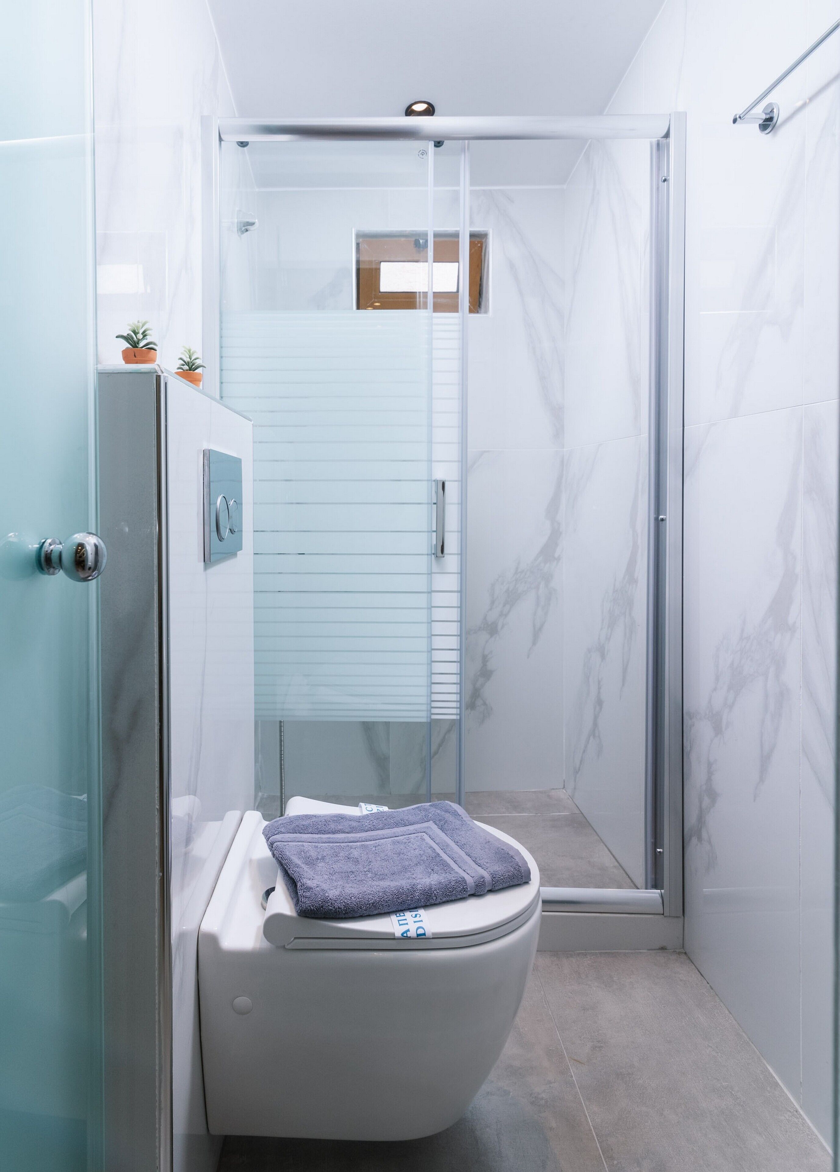 A modern bathroom with a glass shower enclosure, a toilet with a towel, and marble walls.