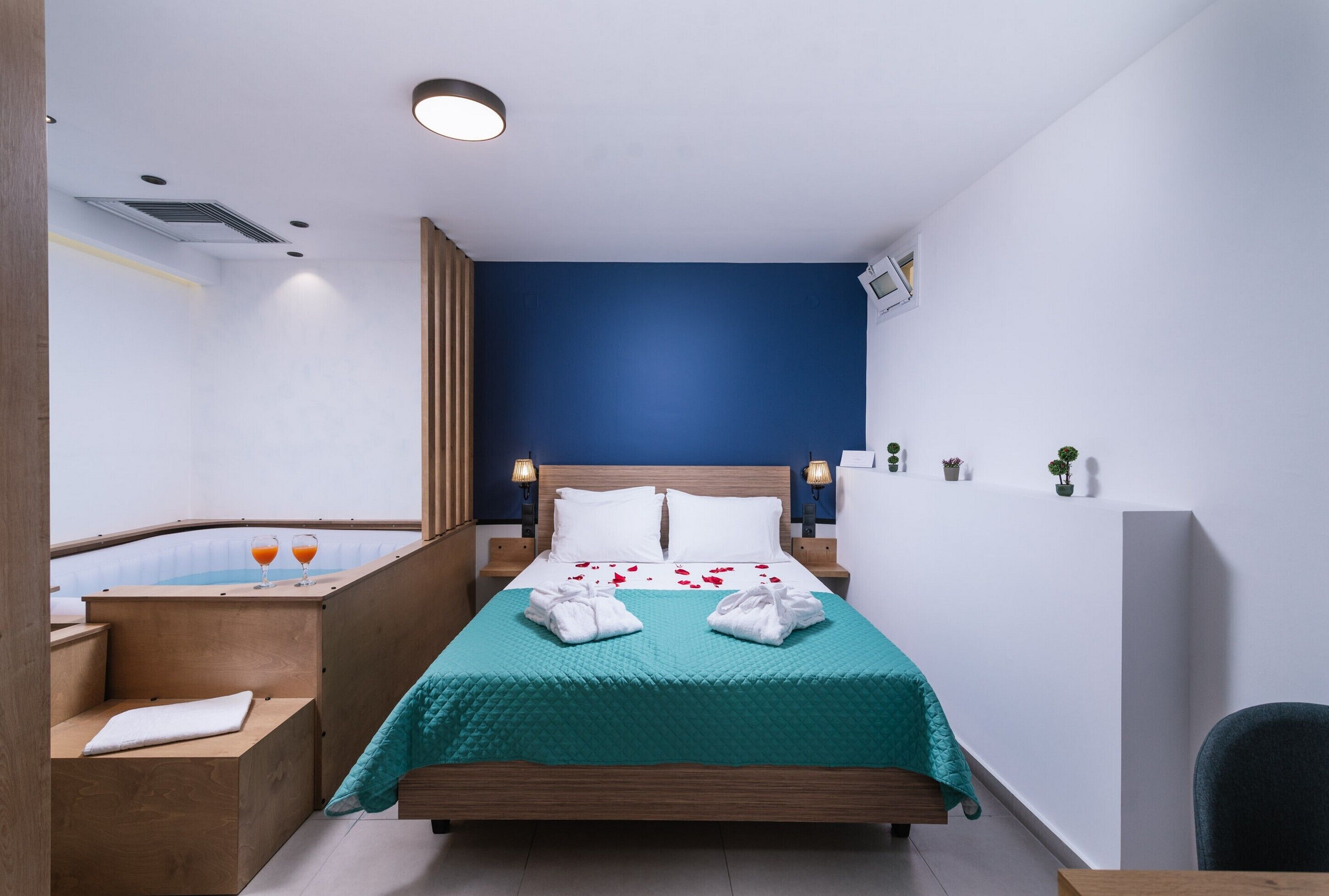 Una habitación de hotel moderna con una cama, un banco de madera, un pequeño rincón de descanso y un televisor fijado a la pared.