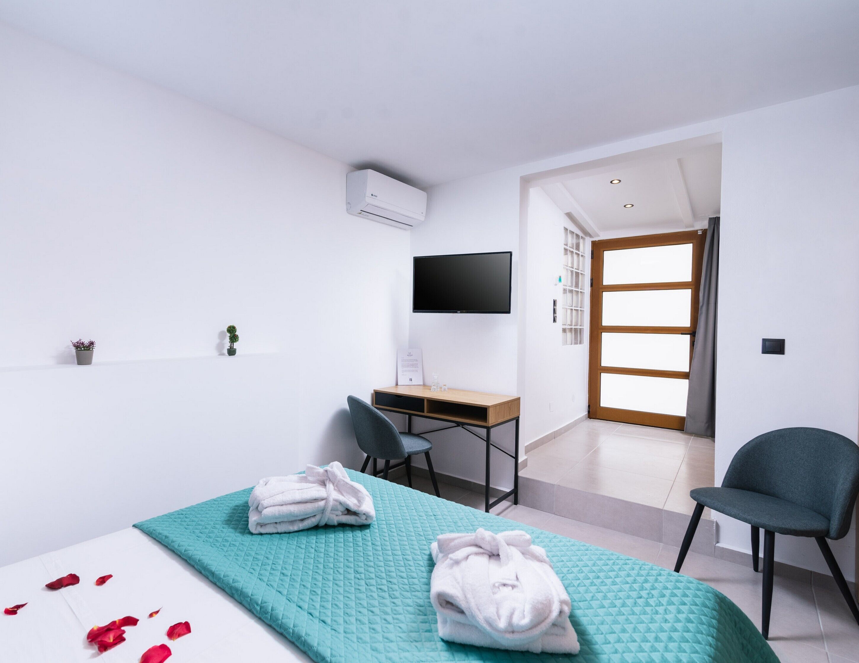 A modern hotel room with a bed, a desk, a chair, a TV, and a door leading to a balcony.