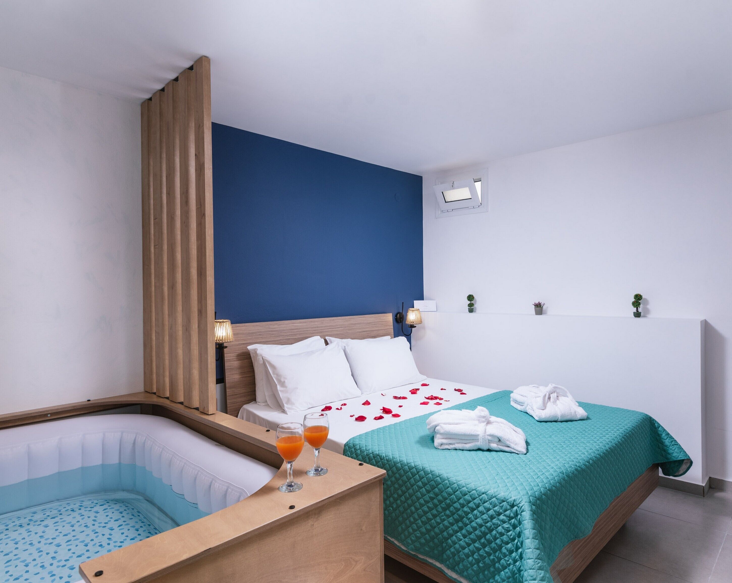 A hotel room with a bed, a wooden headboard, a small bathtub, and a bedside table with a glass of orange juice.