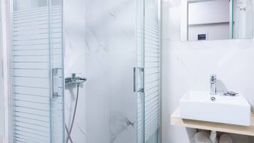 A modern bathroom with a glass-enclosed shower, a white sink, and a mirror above it.