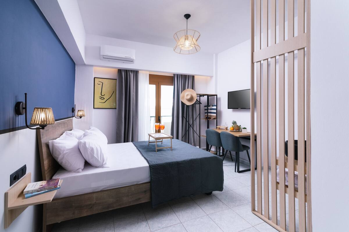 Een moderne hotelkamer met een bed, nachtkastje, lamp en een bureau met stoelen.