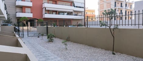 A residential building with multiple balconies, a gated entrance, and a gravel pathway.