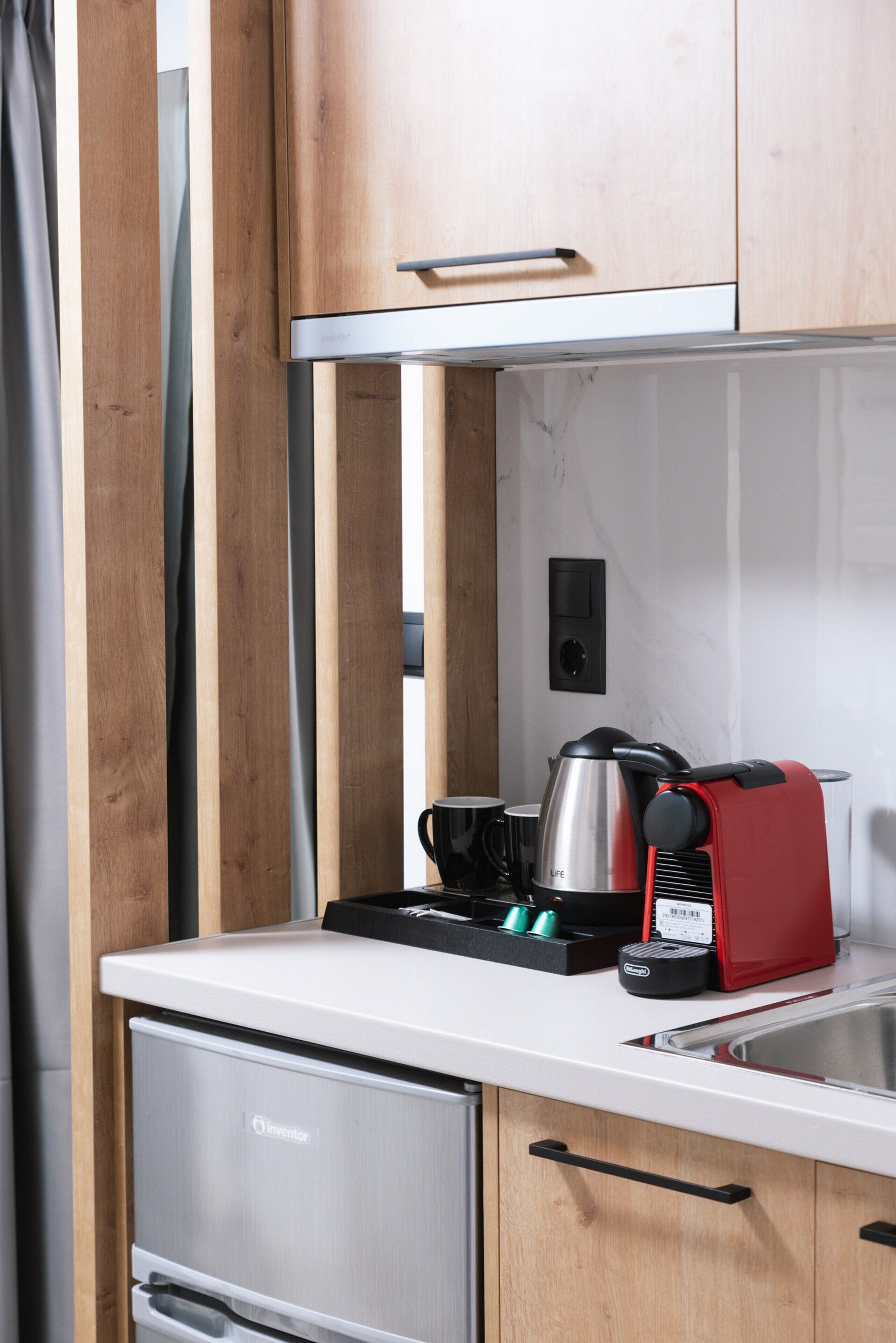 A compact kitchen with a stainless steel refrigerator, a toaster, a kettle, and a coffee maker on the countertop.