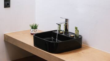 A modern bathroom with a black sink, a round mirror, and a small potted plant on the counter.