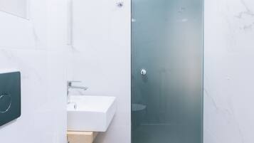 Un baño moderno con cabina de ducha de vidrio, un lavabo blanco y suelo de baldosas de mármol.