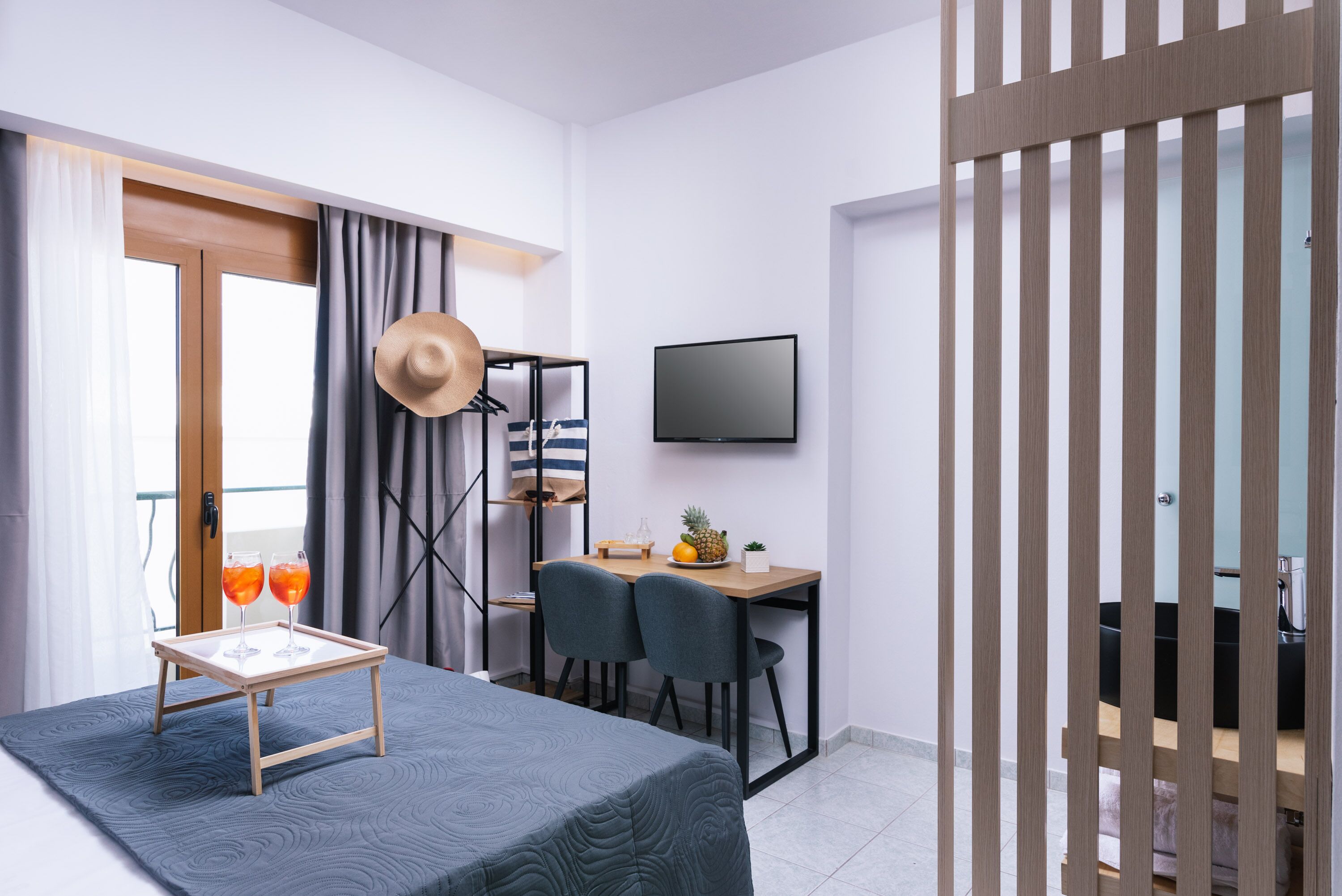 A modern hotel room with a bed, a desk with two chairs, a television, and a wardrobe.