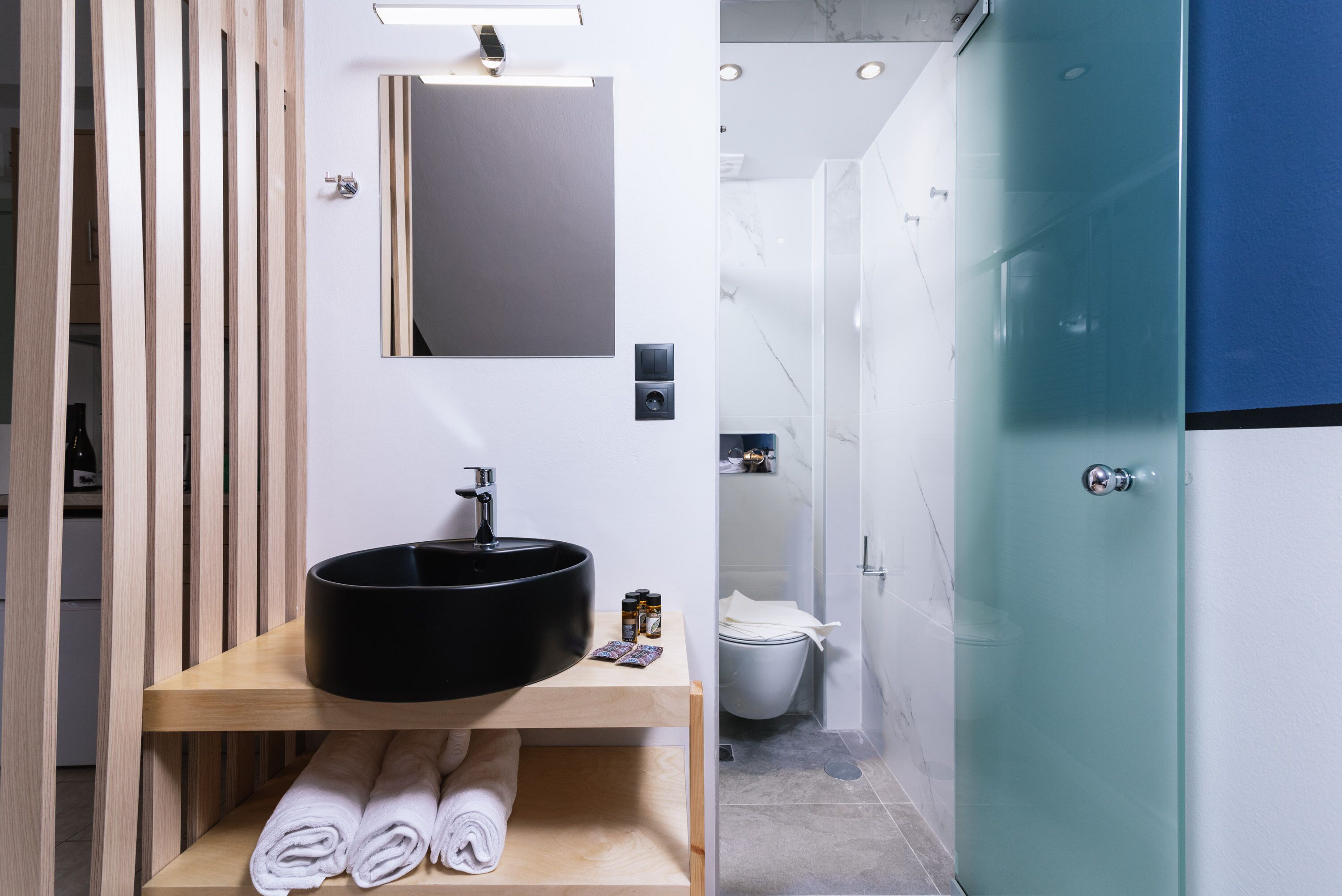 A modern bathroom with a wooden vanity, black sink, and white towels.