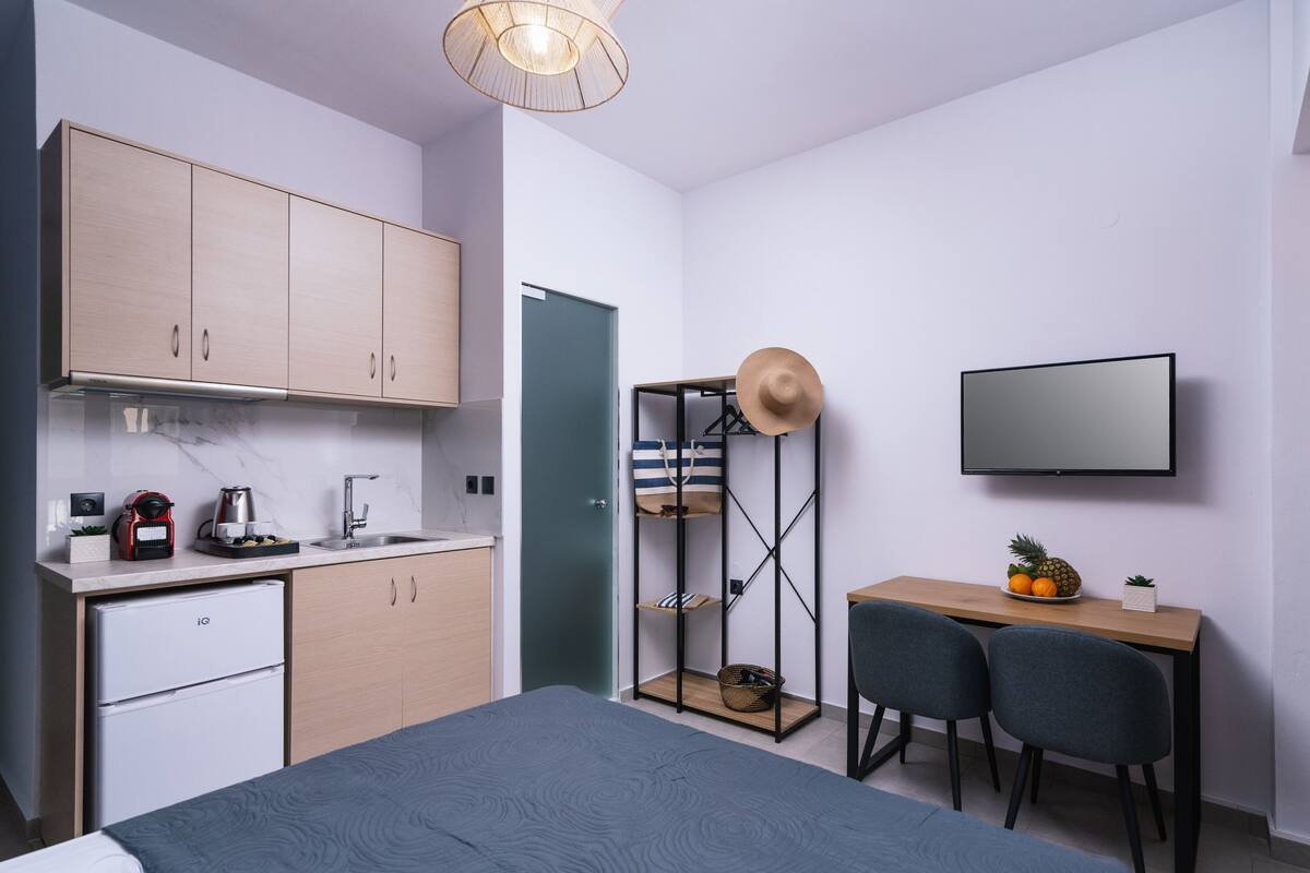 Een compacte slaapkamer met een bed, een bureau met twee stoelen, een televisie en een kledingkast.