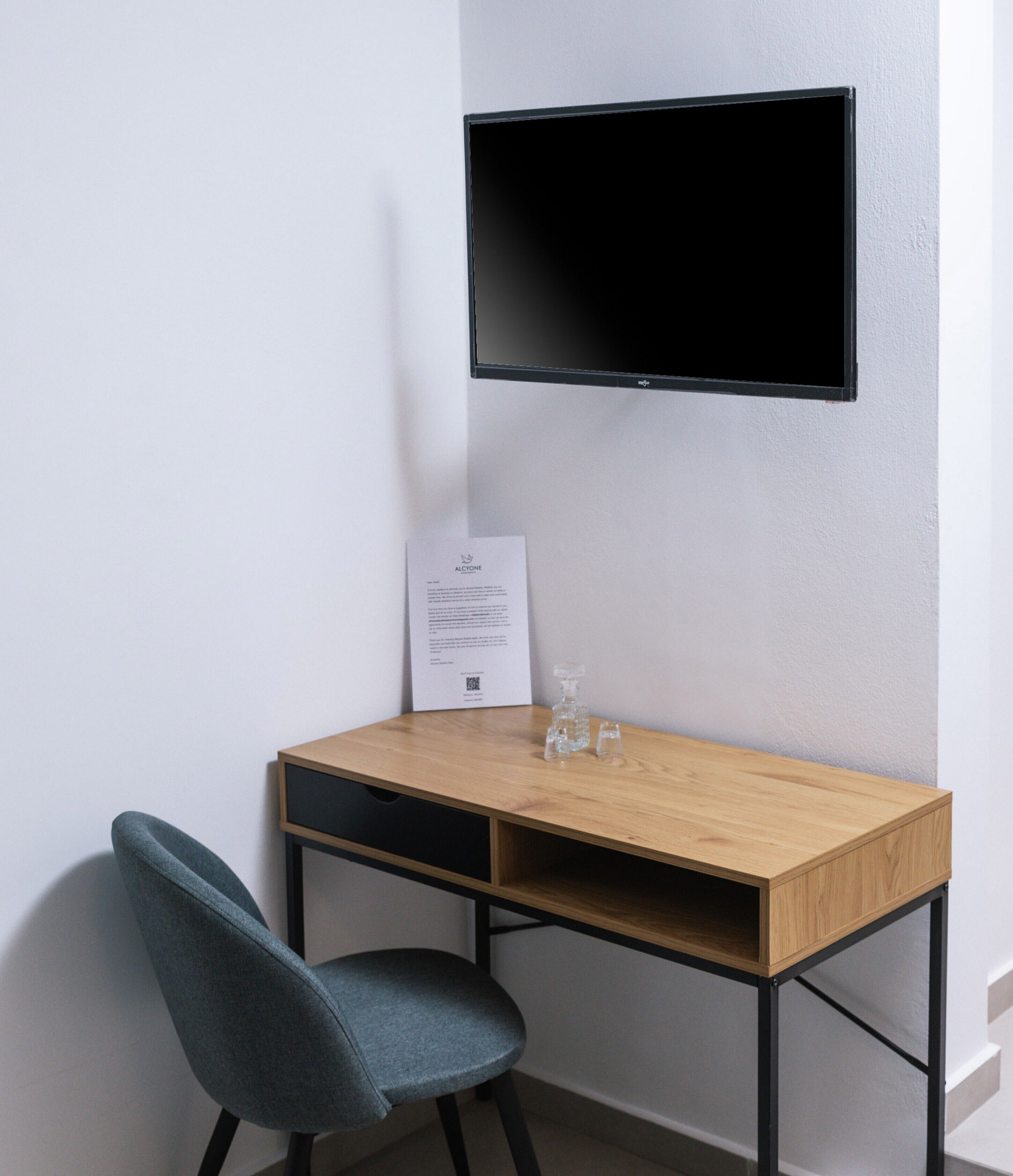 Una habitación moderna con un escritorio de madera, una silla azul, un televisor de pantalla plana montado en la pared y un documento enmarcado sobre el escritorio.