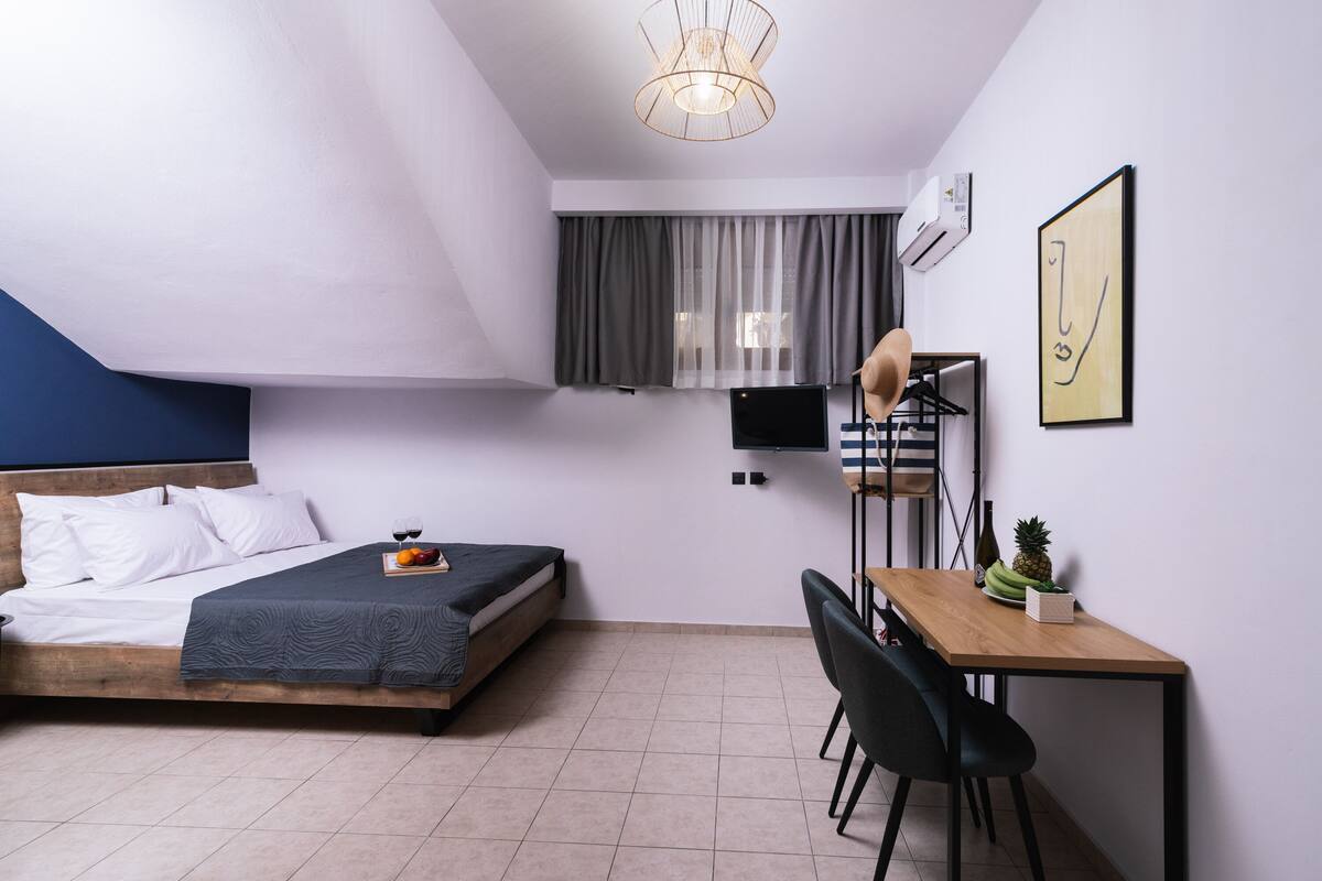 Een slaapkamer met een bed, een bureau en een stoel. Er is een raam met gordijnen, een plafondlamp en een wandairconditioner.