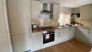 A modern kitchen with white cabinetry, a built-in oven, a microwave, and a toaster. - Cosy Homely Apartment Close to Lincoln City Centre (Lincoln)