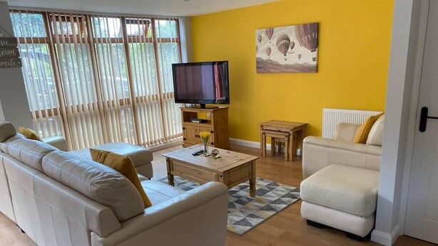 A living room with a sofa, armchair, coffee table, and a TV on a wooden cabinet. - Cosy Homely Apartment Close to Lincoln City Centre (Lincoln)