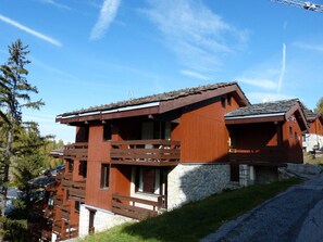 A wooden cabin with a stone foundation, large windows, and a balcony.