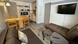 A compact living space with a kitchenette, a dining area, a sofa, and a TV mounted on the wall. - Cozy apartment with balcony, pool and optional parking in Plagne 1800 (La Plagne 1800)