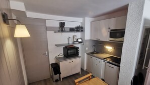 A compact kitchen with a microwave, toaster, and coffee maker on the countertop, a small trash bin, and a wooden table with benches. - Cozy apartment with balcony, pool and optional parking in Plagne 1800 (La Plagne 1800)