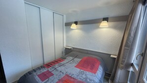 A bedroom with a bed, a wardrobe, and two wall-mounted lights. - Cozy apartment with balcony, pool and optional parking in Plagne 1800 (La Plagne 1800)