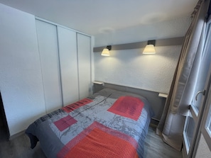 Quarto com cama, guarda-roupa e duas luzes fixadas na parede.