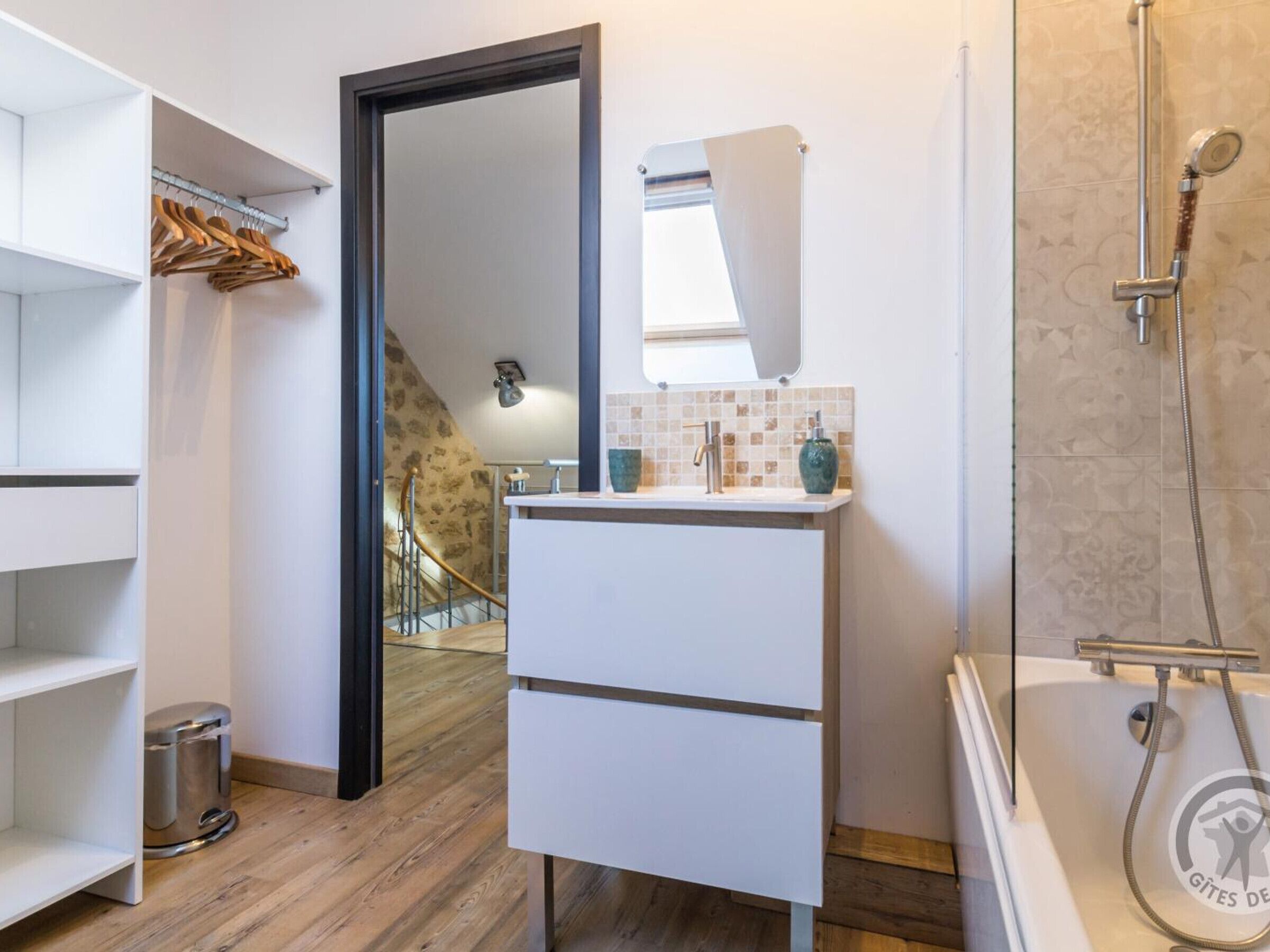 A modern bathroom with a wooden floor, a white sink, a mirror, and a shower.
