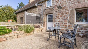 A stone house with a tiled roof, a gravel patio, and two metal chairs. - Cozy Seaside Cottage with Terrace, Private Garden & Electric Car Charging (Vicq-sur-Mer)