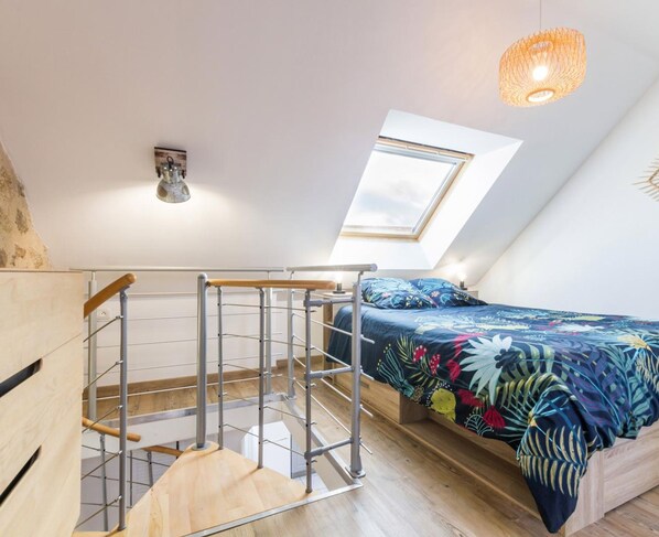 A bedroom with a skylight, a bed with a floral bedspread, a wooden ladder, and a hanging light fixture.