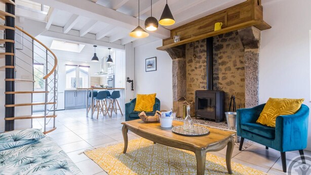 A spacious living room with a wooden coffee table, two blue armchairs, a fireplace, and a kitchen in the background. - Cozy Seaside Cottage with Terrace, Private Garden & Electric Car Charging (Vicq-sur-Mer)