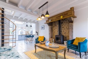 A spacious living room with a wooden coffee table, two blue armchairs, a fireplace, and a kitchen in the background.