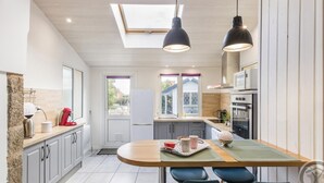 A modern kitchen with a skylight, two pendant lights, a dining area with a table and chairs, and a view of the outside. - Cozy Seaside Cottage with Terrace, Private Garden & Electric Car Charging (Vicq-sur-Mer)
