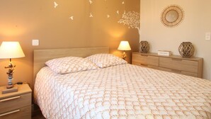 A bedroom with a bed, two bedside tables with lamps, a dresser, a wall decal of birds, and a round mirror. - Charming house with enclosed garden in Cotentin Marshes (Liesville-sur-Douve)